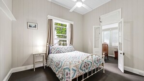 Een slaapkamer met een bed, een nachtkastje, een raam met gordijnen, een deur en een plafondventilator.