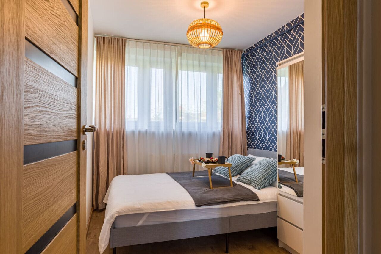 A modern bedroom with a bed, bedside table, and a large window with curtains.