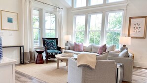 A living room with a grey sofa, a patterned armchair, and a coffee table. There are two lamps on either side of the sofa. - NEW!—IBIS COTTAGE—Beach side retreat. Prime location with Bikes and Beach gear! (Oak Island)