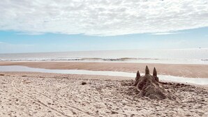 A sandy beach with footprints leading to a sandcastle. - NEW!—IBIS COTTAGE—Beach side retreat. Prime location with Bikes and Beach gear! (Oak Island)