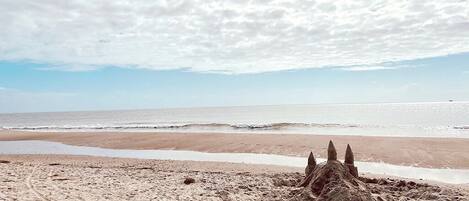 A sandy beach with footprints leading to a sandcastle.