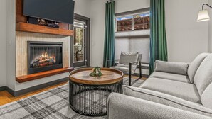 Ein Wohnzimmer mit Kamin, einem flachbildfernseher darüber und einem runden Couchtisch sowie einem Sofa.