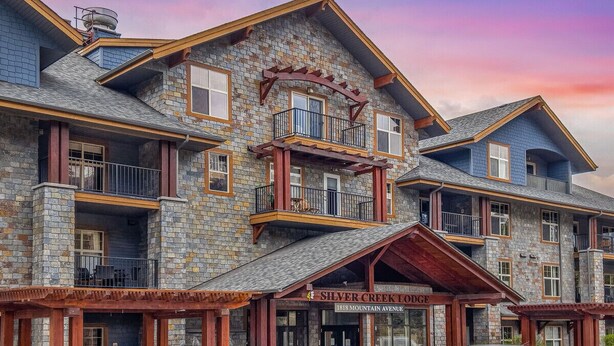 Ein mehrstöckiges Loghaus mit Steinaußenwand, Balkonen und einem markanten Eingang, der mit "Silver Creek Lodge" beschriftet ist.
