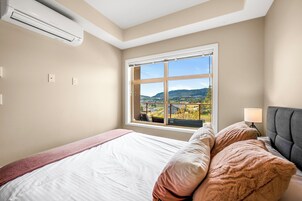 Un dormitorio con una cama grande, una ventana con vistas al campo, un equipo de aire acondicionado y una lámpara de noche.