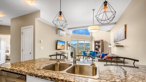 A modern kitchen with granite countertops, stainless steel sinks, and pendant lighting. - Top Floor Condo at Amenity Rich Resort (West Kelowna)