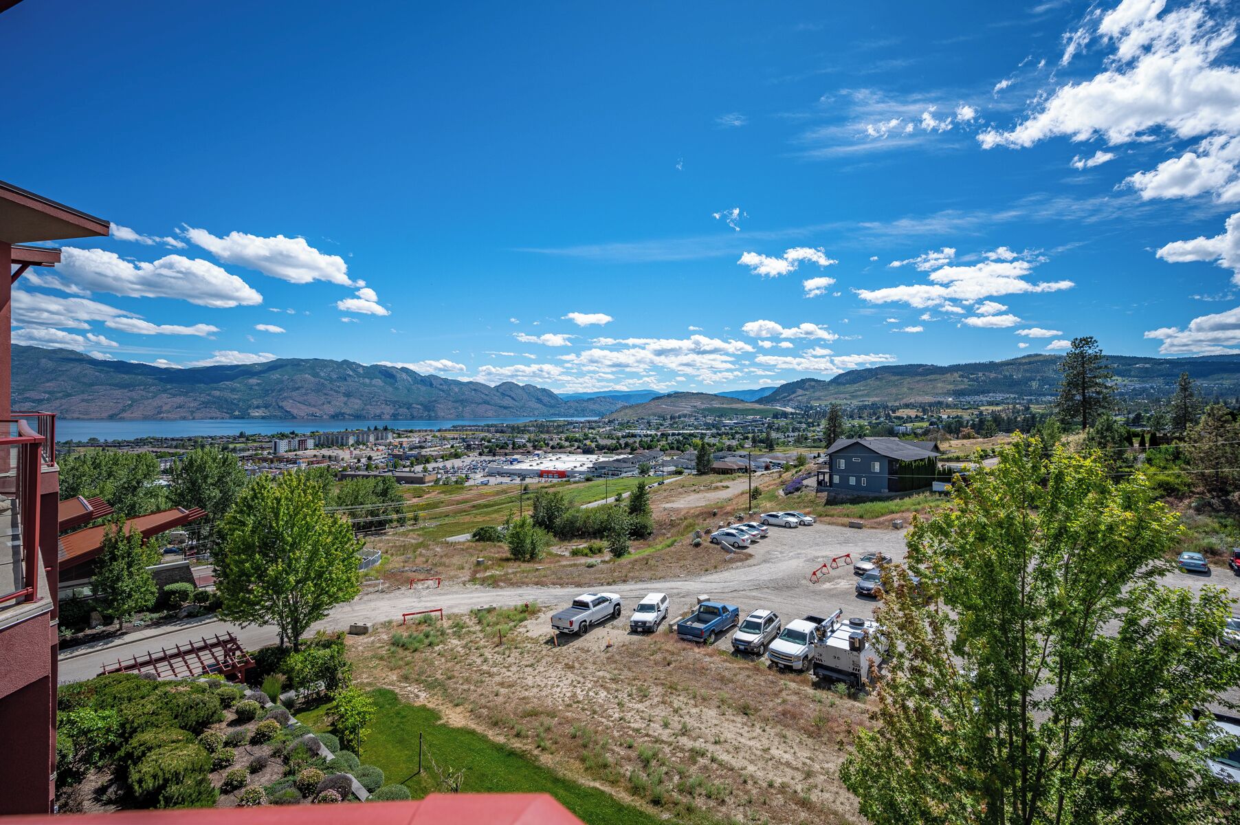 A view of a parking lot with several cars, a small building, and a mountainous landscape in the background.