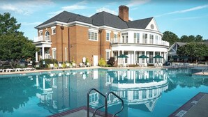 A large pool with a reflection of a building, surrounded by lounge chairs and umbrellas.