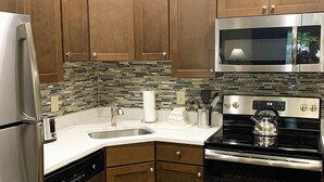 A kitchen with stainless steel appliances, wooden cabinets, and a tiled backsplash.