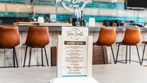 Un espace bar avec un présentoir pour la carte des boissons, des tabourets de bar et un panneau néon indiquant « Blue Smith ».