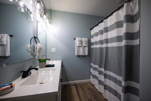 Une salle de bain avec un lavabo blanc, un miroir et un rideau de douche à rayures.