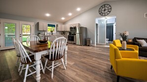 Una cocina moderna con armarios blancos, un refrigerador de acero inoxidable y un comedor con una mesa de madera y sillas blancas.