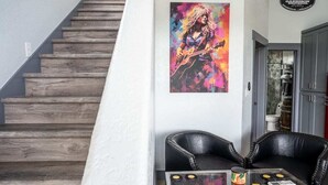 A staircase with wooden steps, a black leather sofa, a glass coffee table with a guitar, and a colorful painting on the wall. - HACIENDA AMOR Summary (Johnson City)