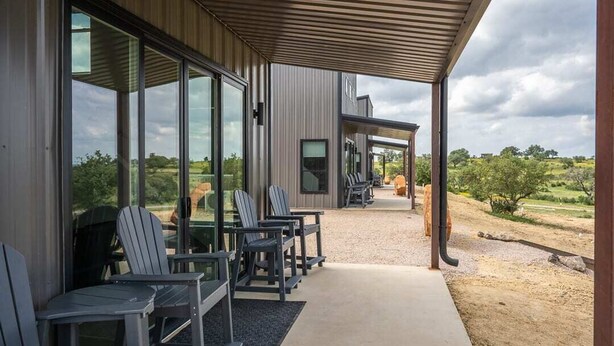 An outdoor seating area with chairs and tables, a covered walkway, and a view of the countryside. - HACIENDA AMOR Summary (Johnson City)