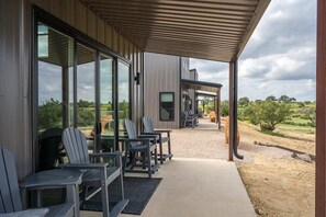 An outdoor seating area with chairs and tables, a covered walkway, and a view of the countryside. - HACIENDA AMOR Summary (Johnson City)