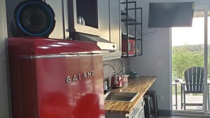 A kitchen with a red Galanz refrigerator, a microwave, and a sink. There is a wooden countertop and a chair near the window. - HACIENDA AMOR Summary (Johnson City)