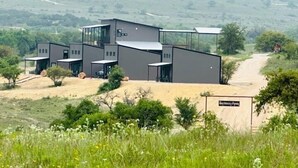 A modern building with a flat roof and large windows, surrounded by a grassy field and a dirt path. - HACIENDA AMOR Summary (Johnson City)
