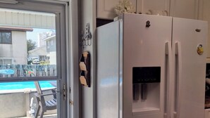 Eine Küche mit einem weißen Kühlschrank, einer Tür, die auf einen Balkon mit einem Pool führt, und einer kleinen Leiter.