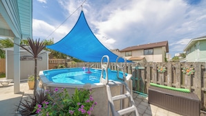 Ein Garten mit Schwimmbecken, einem blauen Sonnensegel und einem Holzzaun.