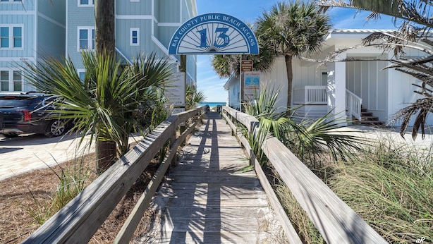 Ein hölzerner Steg führt zu einem Gebäude, an dem ein Schild mit der Aufschrift "Bay County Public Beach Access" steht.