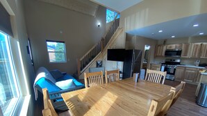 Amplia sala de estar con una gran mesa de comedor de madera, un sofá y una escalera que sube a un nivel superior.