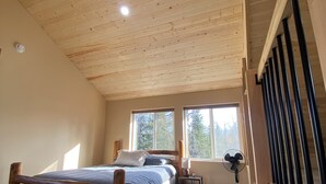 Un dormitorio con techo de madera, cama, ventana y ventilador.