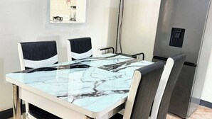 A dining area with a marble table, four chairs, a refrigerator, and a window with kitchen appliances visible. - Eagle Weavers Nest (Livingstone)