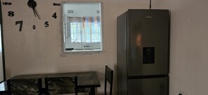 A kitchen with a stainless steel refrigerator, a window with curtains, and a wall clock. - Eagle Weavers Nest (Livingstone)