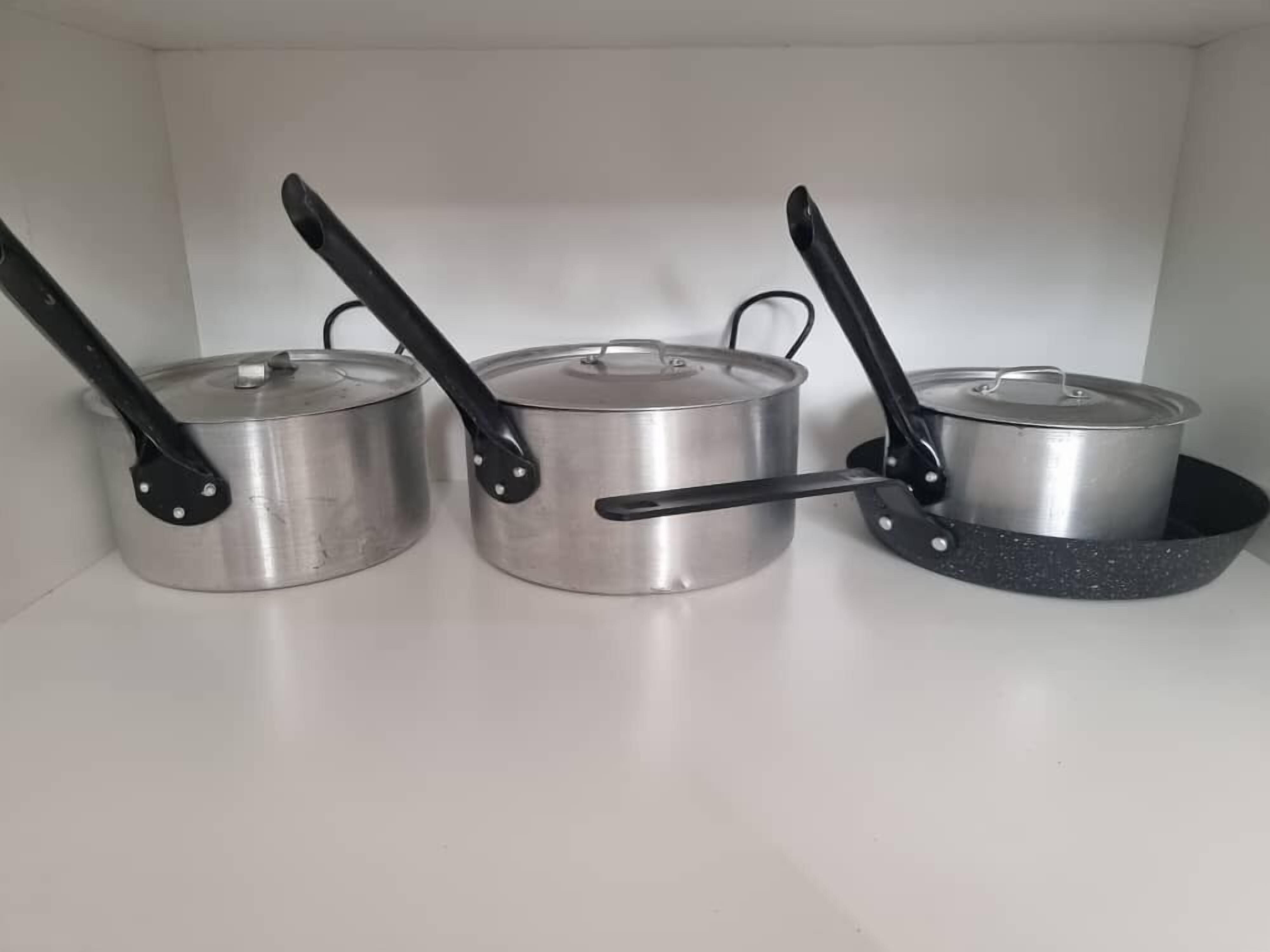 Three stainless steel pots with black handles on a white shelf.