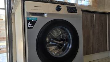 Una lavadora de carga frontal Hisense A+++ de 6kg en una cocina con armarios de madera y un ventanal.