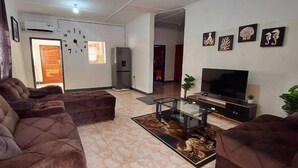 A living room with a large brown sofa set, a glass coffee table, a flat-screen TV, and a refrigerator. - Eagle Weavers Nest (Livingstone)