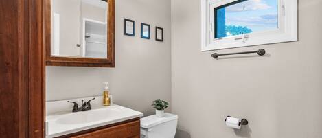 A bathroom with a wooden vanity, a white sink, a toilet, a mirror, and a window with a view of trees.