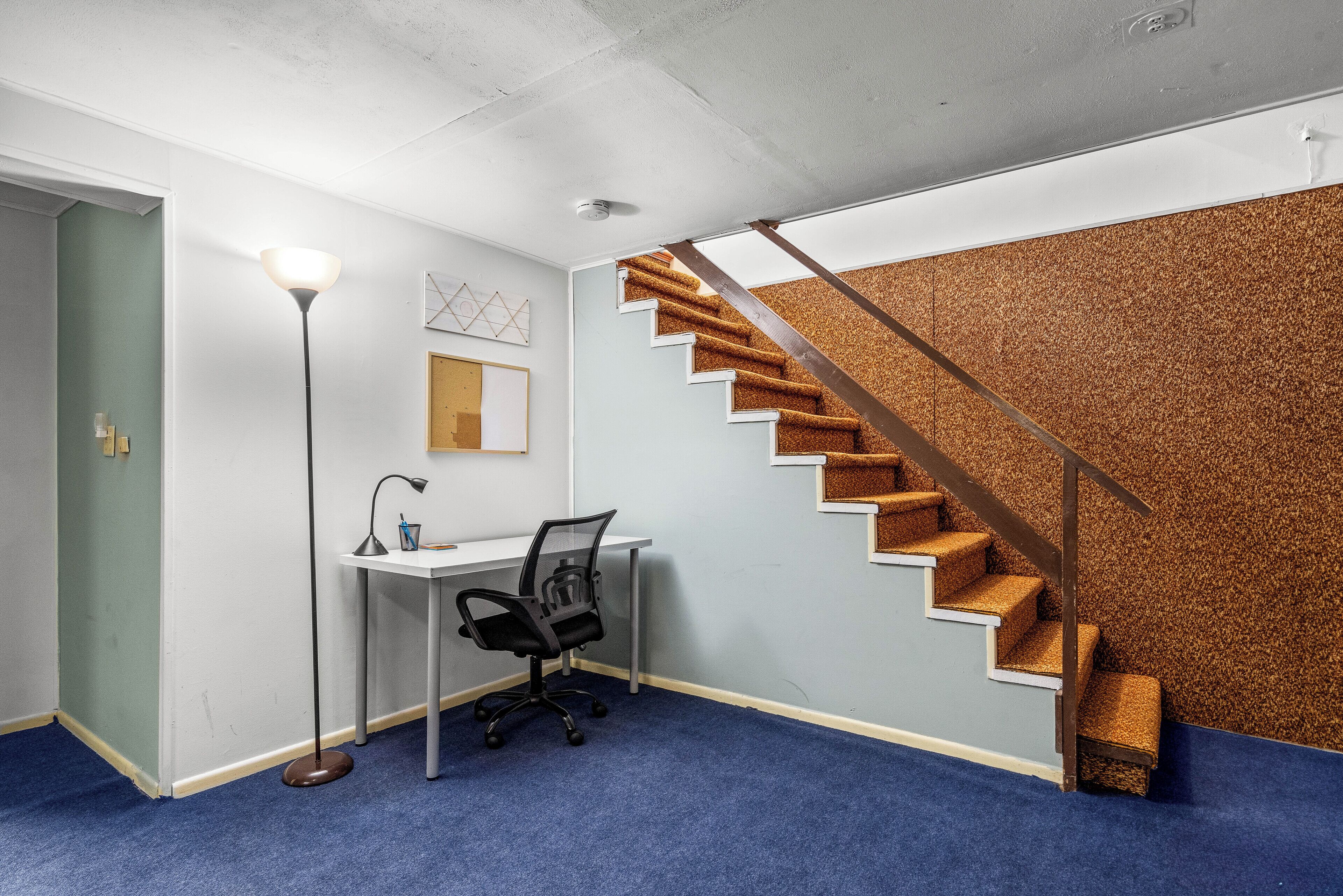 Ein Zimmer mit Schreibtisch, Stuhl und einer Treppe mit Holzstufen und Metallgeländern.