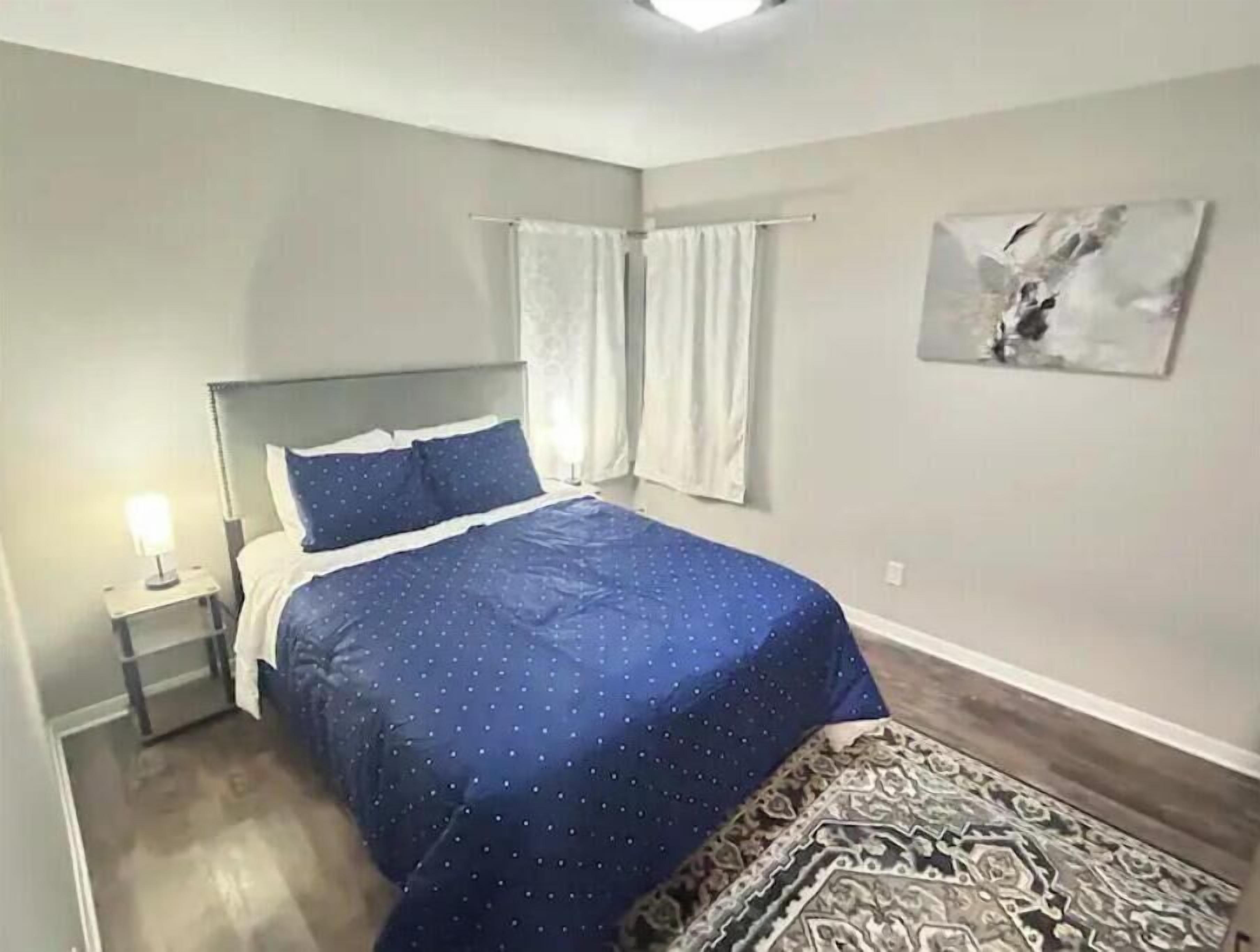 Een slaapkamer met een bed, nachtkastje, raam met gordijnen en een wanddecoratie.