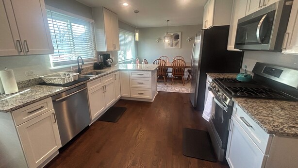 A modern kitchen with white cabinets, a stainless steel refrigerator, a microwave, and a gas stove.