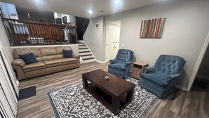 A living room with a brown leather sofa, two blue armchairs, a dark coffee table, and a patterned rug.