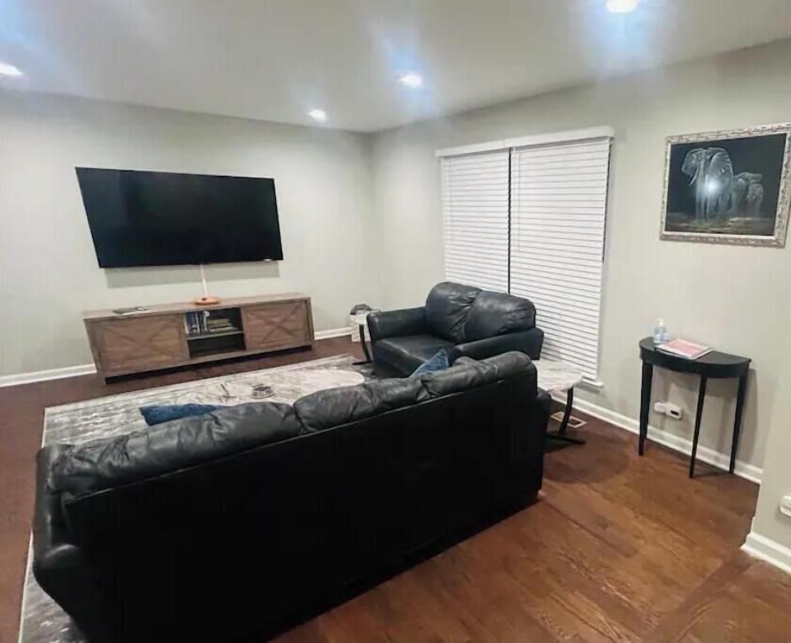 A living room with a black leather sofa, a flat-screen TV mounted on the wall, a wooden cabinet, and a framed picture on the wall.