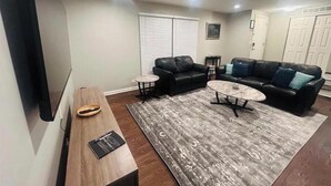 A modern living room with a wooden bench, two black leather sofas, a marble coffee table, and a grey patterned rug.