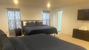 A bedroom with two beds, a TV on the wall, and a bedside table with a lamp.