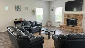 A living room with a stone fireplace, leather sofas, a flat-screen TV, and a small table.