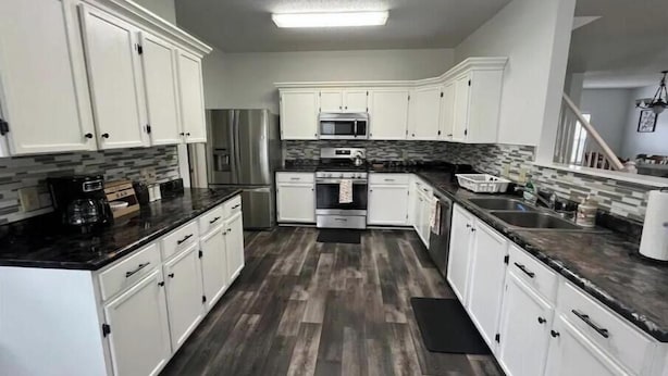 A modern kitchen with white cabinets, a stainless steel refrigerator, a microwave, and a stove.