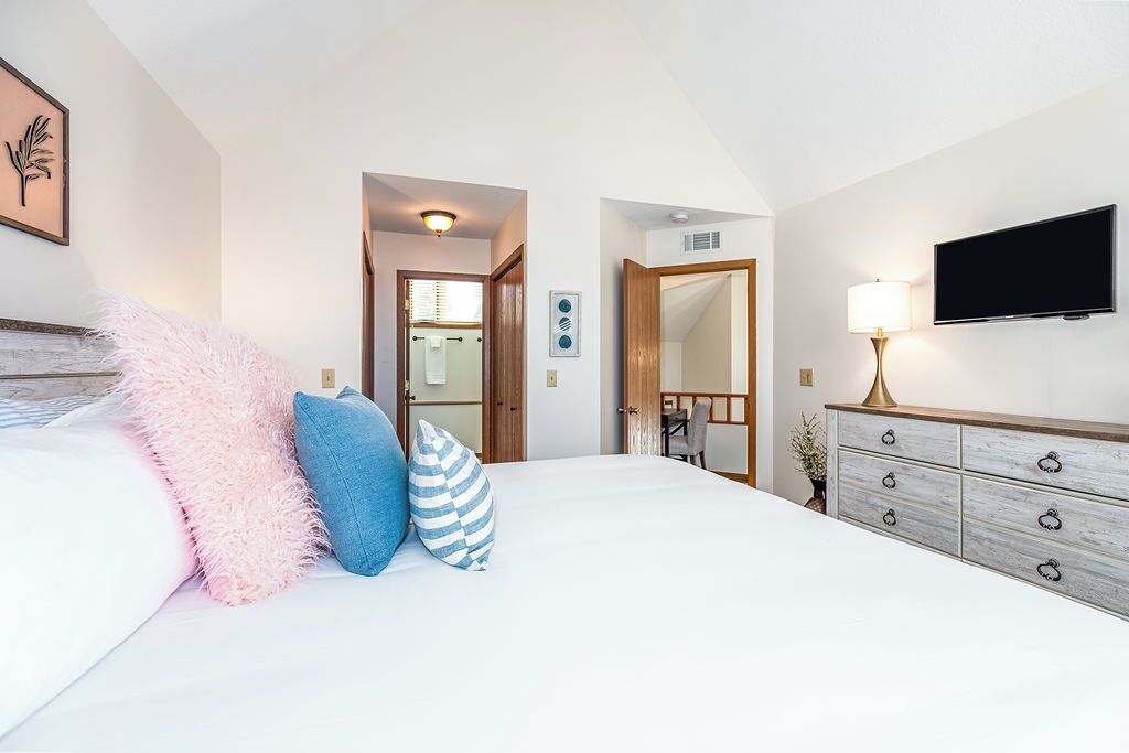 Une chambre d’hôtel avec un grand lit, une commode en bois, une télévision et un miroir.