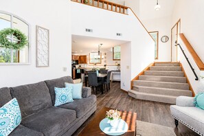 A modern living room with a grey sofa, a coffee table, and a staircase leading to an upper level. - Serene 2-King Golf Villa ~ Fireplace + Spa Nearby (Galena)
