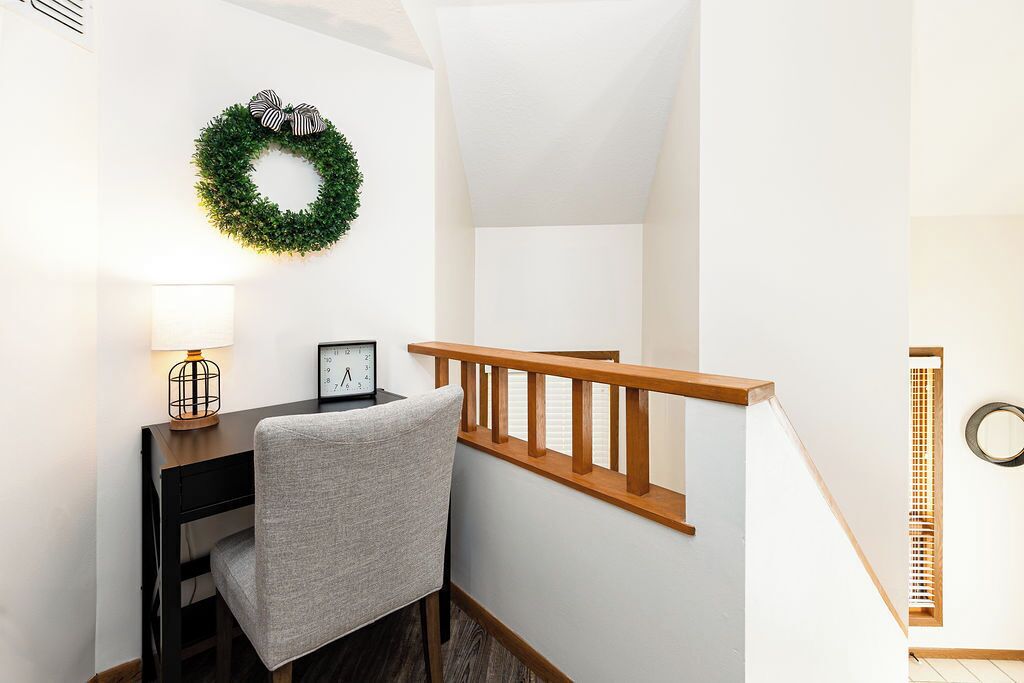 Un escalier avec une rampe en bois, un bureau avec une chaise, une horloge murale et une couronne de fleurs.
