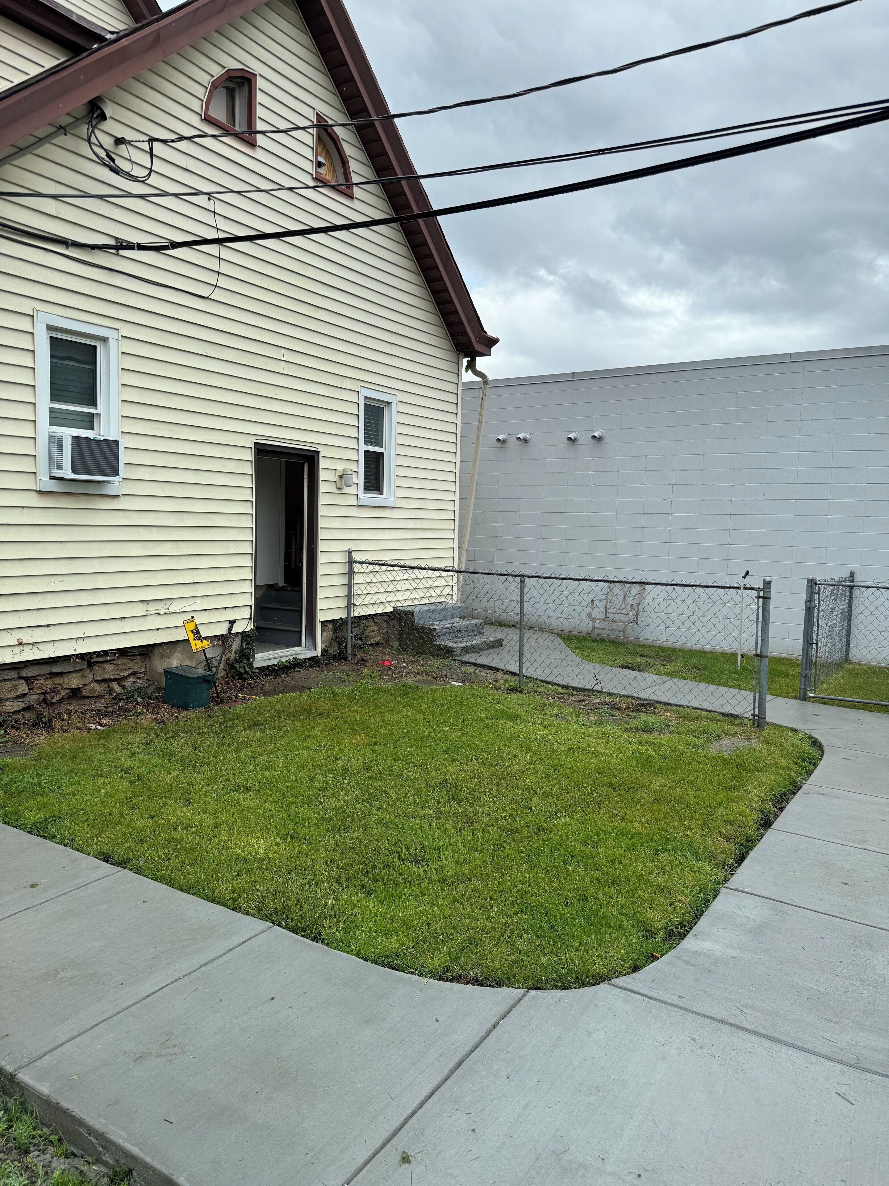 A residential house with a small lawn, a chain-link fence, and a concrete pathway.