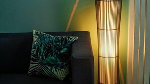 A modern living room with a dark sofa, a decorative pillow, and a tall floor lamp against a teal wall with framed pictures.