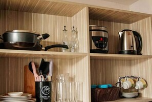 Una cocina con estantes de madera, una cafetera, un hervidor y utensilios de cocina.