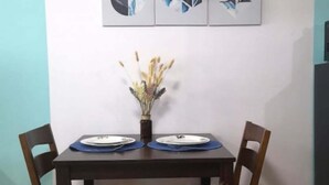 A dining area with a table set for two, a vase with dried flowers, and abstract art on the wall.