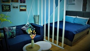 A room with a blue sofa, a bed with blue bedding, and a small round table with a vase of flowers.