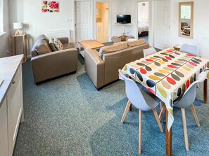 A compact living space with a sofa, a dining table with chairs, a television, and a bed in the background. - Lily Pad 4 - UK43910 (Nassington, near Stamford)