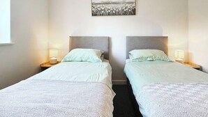 A hotel room with two beds, each with a headboard, bedside lamps, and a wall-mounted picture.